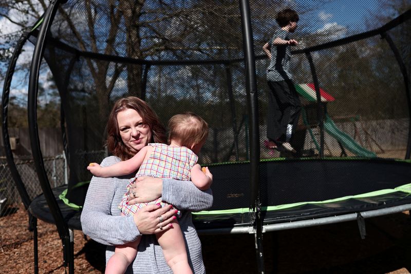 &copy; Reuters. Kristia holds her youngest child in her arms while her eldest child jumps on the backyard trampoline, in Birmingham, Alabama, U.S., February 23, 2024. Kristia Rumbley of Birmingham used in vitro fertilization to have three children, and has kept two embry