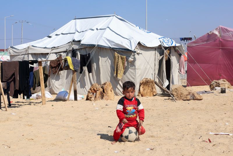 &copy; Reuters. Un garçon palestinien déplacé, qui a fui sa maison à cause des frappes israéliennes, est assis sur un ballon, dans un camp de tentes, près de la frontière avec l'Égypte, à Rafah, dans le sud de la bande de Gaza. /Photo prise le 25 février 2024.R