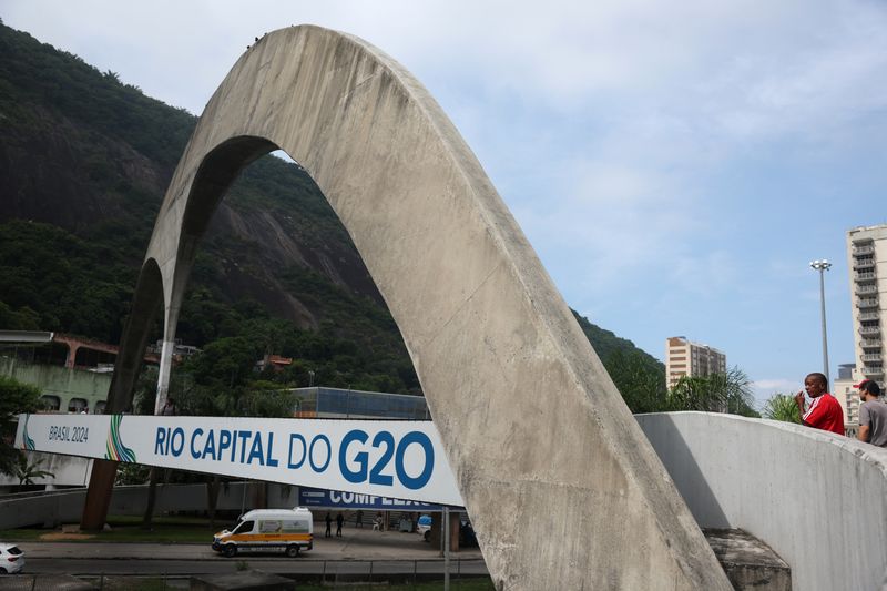 &copy; Reuters. مارة بحي روسينيا الفقير في ريو دي جانيرو يسيرون إلى جانب لافتة تشير إلى قمة مجموعة العشرين في البرازيل. التقطت الصورة يوم 21 فبراير شباط 2024. ت