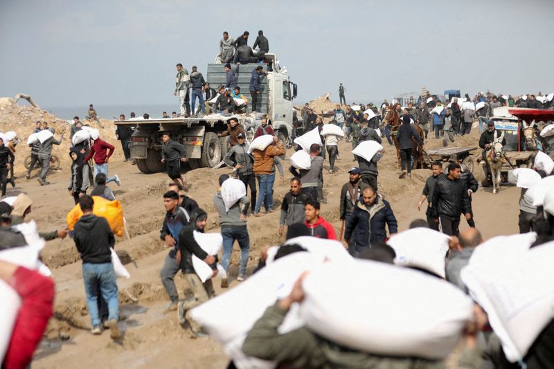 &copy; Reuters. Palestinos carregam sacos de farinha que pegaram de caminhão de ajuda perto de posto de controle israelense na Cidade de Gaza
19/02/2024
REUTERS/Kosay Al Nemer