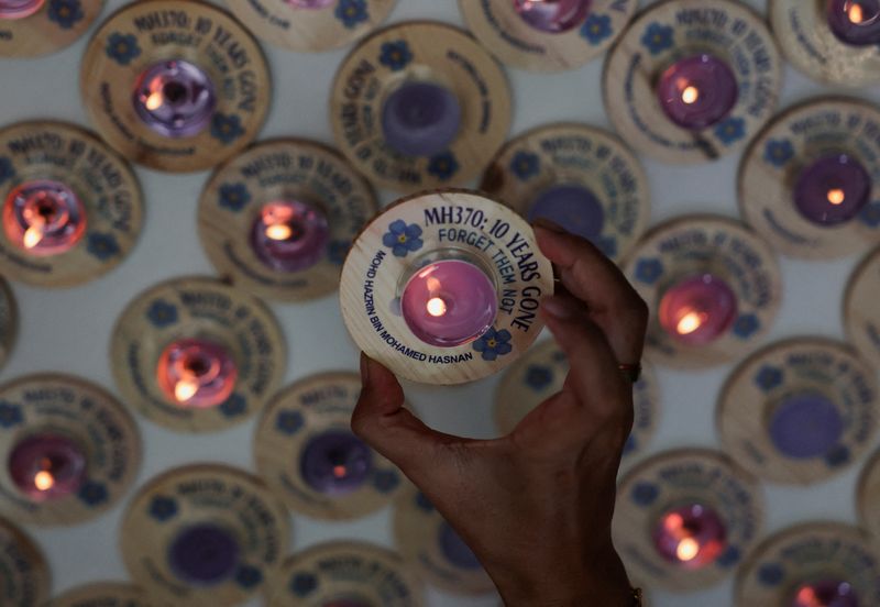 &copy; Reuters. فرد من أسرة مضيف طيران كان على متن الرحلة إم.إتش370 الماليزية المفقودة يحمل شمعة عليها اسمه خلال فعالية بمناسبة الذكرى العاشرة لاختفاء الطائ