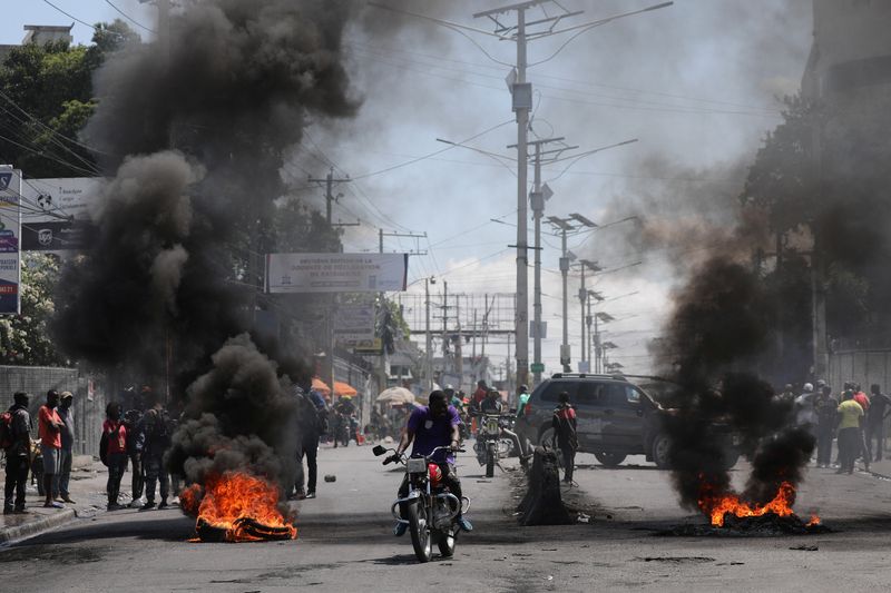 © Reuters. Motorists pass by a burning barricade during a protest as the government said it would extend a state of emergency for another month after an escalation in violence from gangs seeking to oust the Prime Minister Ariel Henry, in Port-au-Prince, Haiti, March 7, 2024. REUTERS/Ralph Tedy Erol