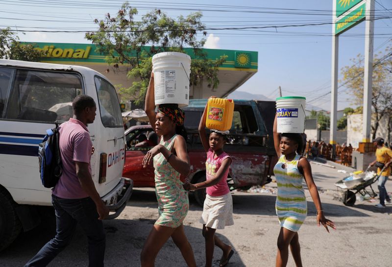 &copy; Reuters. Mujeres transportan agua en cubos y contenedores por una calle después de que el primer ministro de Haití, Ariel Henry, se comprometió a dimitir tras meses de escalada de la violencia de bandas, en Puerto Príncipe, Haití. 12 de marzo de 2024. REUTERS