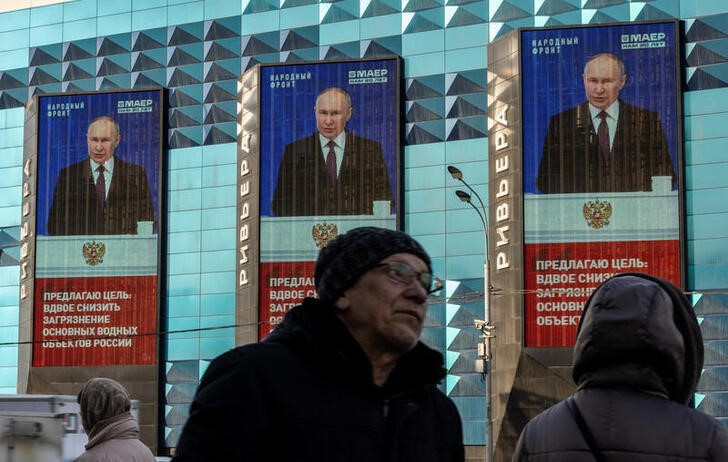 © Reuters. People wait for a bus next to electronic screens on the facade of a building showing an image of Russian President Vladimir Putin and a quote from his address to the Federal Assembly, in Moscow, Russia, February 29, 2024. REUTERS/Maxim Shemetov/files