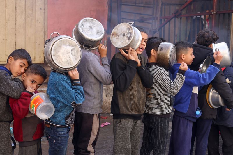 &copy; Reuters. Bambini palestinesi trasportano pentole mentre fanno la fila per ricevere cibo cucinato da una cucina di beneficenza, data la carenza di scorte alimentari, mentre continua il conflitto tra Israele e Hamas, a Rafah, nel sud della Striscia di Gaza, il 14 di