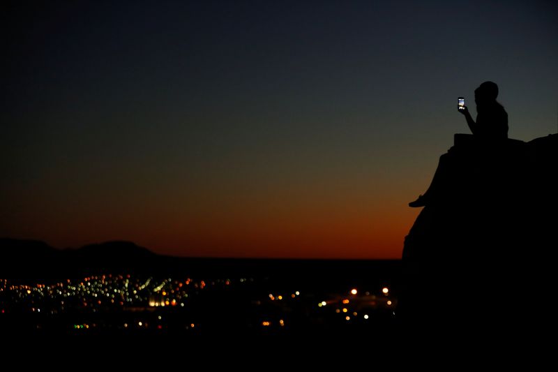 © Reuters. A young couple look at their phone as they sit on a hillside after sun set in El Paso, Texas, U.S., June 20, 2018.        REUTERS/Mike Blake