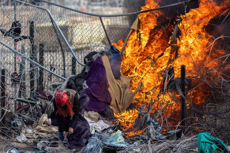 &copy; Reuters. A migrant checks her bag after members of the Texas National Guard burnt clothing used by migrants to break through razor wire and a fence to enter the U.S. to surrender themselves, as SB 4 law that would empower law enforcement authorities in the state t