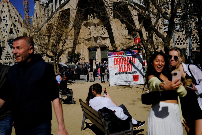 &copy; Reuters. Turistas junto a un cartel en la Basílica de la Sagrada Familia que alerta de la grave sequía en la región noreste de España e insta a ahorrar agua debido a los bajos niveles de los embalses, en un momento en que Cataluña declara el estado de emergen
