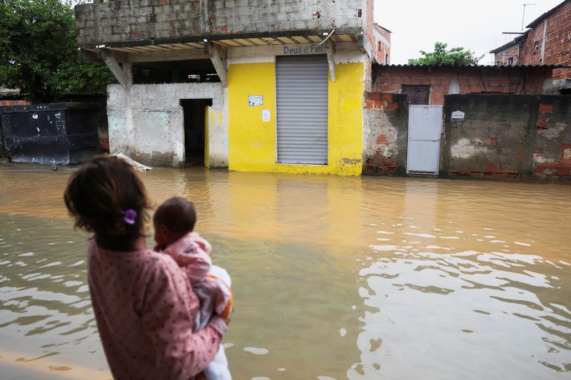 &copy; Reuters. Mulher com criança de colo observa rua inundada após fortes chuvas em Duque de Caxias, no Rio de Janeiro
24/03/2024 REUTERS/Pilar Olivares