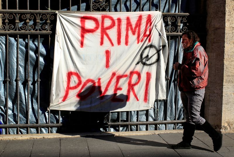 &copy; Reuters. FILE PHOTO: Angela Grossi walks past a banner reading "Poor first", hanging in a gate of the portico of the Basilica of the Santi Apostoli, where she lives after being evicted from an unused building along with other families in August 2017, in Rome, Ital