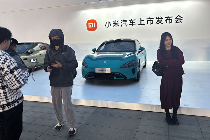 © Reuters. People pose for pictures in front of Xiaomi's first electric vehicle SU7 that is displayed outside the avenue for the car's launch event in Beijing, China March 28, 2024. REUTERS/Sarah Wu