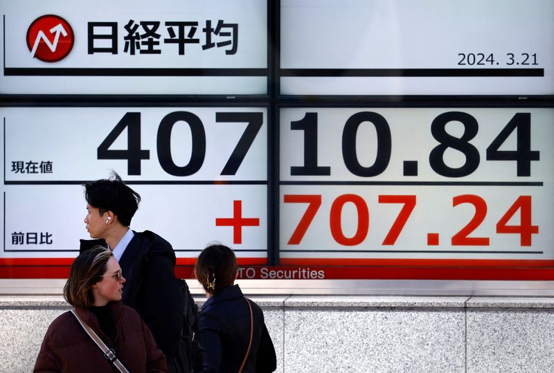 © Reuters. Passersby walk in front of an electric screen displaying Japan's Nikkei share average outside a brokerage in Tokyo, Japan March 21, 2024.  REUTERS/Issei Kato/File Photo