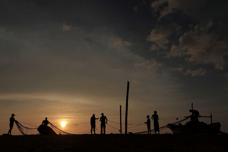 &copy; Reuters. Men are silhouetted as they clear a fish net on a beach in Colombo, Sri Lanka January 21, 2021. REUTERS/Dinuka Liyanawatte/File Photo