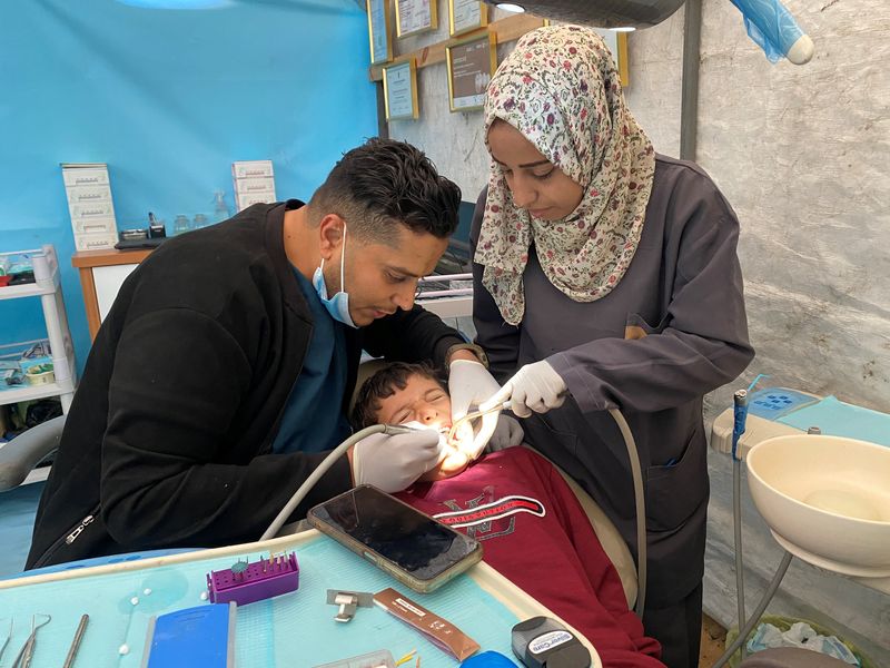 © Reuters. طبيب الأسنان الفلسطيني نجدت صقر الذي دمر القصف الإسرائيلي عيادته يعالج مرضاه داخل خيمة بمخيم النصيرات في قطاع غزة يوم 30 مارس آذار 2024. تصوير: دعاء روقة - رويترز