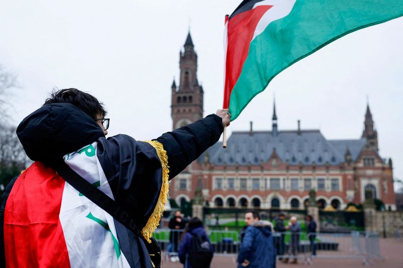 &copy; Reuters. Un uomo sventola una bandiera palestinese durante le proteste nel giorno dell'udienza pubblica tenuta dalla Corte internazionale di giustizia (Cig) per consentire alle parti di esprimere il proprio parere sulle conseguenze legali dell'occupazione israelia
