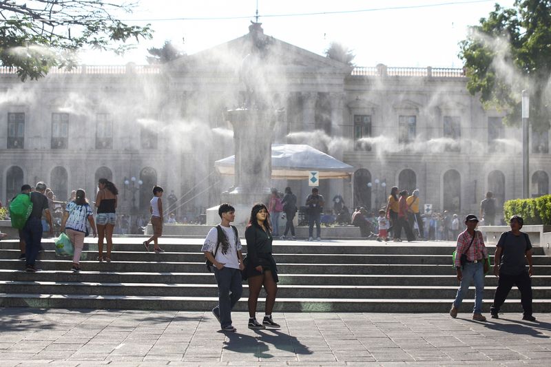 © Reuters. People walk as water is sprayed by a system to alleviate the high temperatures caused by a heat wave, at the Gerardo Barrios square, in San Salvador, El Salvador, March 27, 2024. REUTERS/Jose Cabezas/File Photo