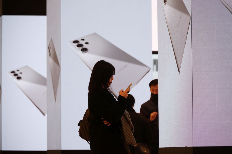 © Reuters. FILE PHOTO: A woman uses her mobile phone in front of electronic boards promoting Samsung Electronics' new flagship smartphones Galaxy S24 series in Seoul, South Korea, January 18, 2024.   REUTERS/Kim Hong-Ji