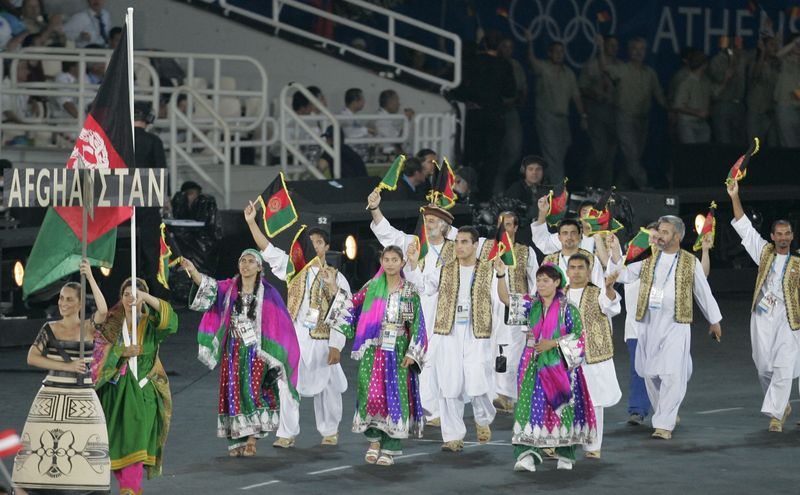 &copy; Reuters. FOTO DE ARCHIVO: La afgana Nina Suratger (segunda a la izquierda) sostiene la bandera nacional de Afganistán delante de los miembros del equipo nacional durante la ceremonia de apertura de los Juegos Olímpicos de Atenas 2004. 13 de agosto de 2004. REUTE