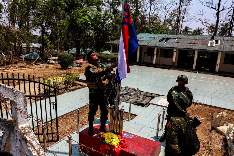 &copy; Reuters. ４月１５日、ミャンマー東部カレン州ミャワディを先週制圧した武装勢力は、同地の国軍基地で軍事政権が使っていた旗を焼き、自らの横断幕を掲げた。写真は旗を掲げる「カレン民族同盟