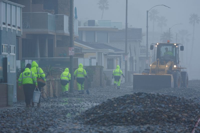 © Reuters. Work crews clean up a beach front road after ocean waves caused by a winter storm pushed up beach rocks in Oceanside, California, U.S., February 20, 2024.  REUTERS/Mike Blake/File Photo