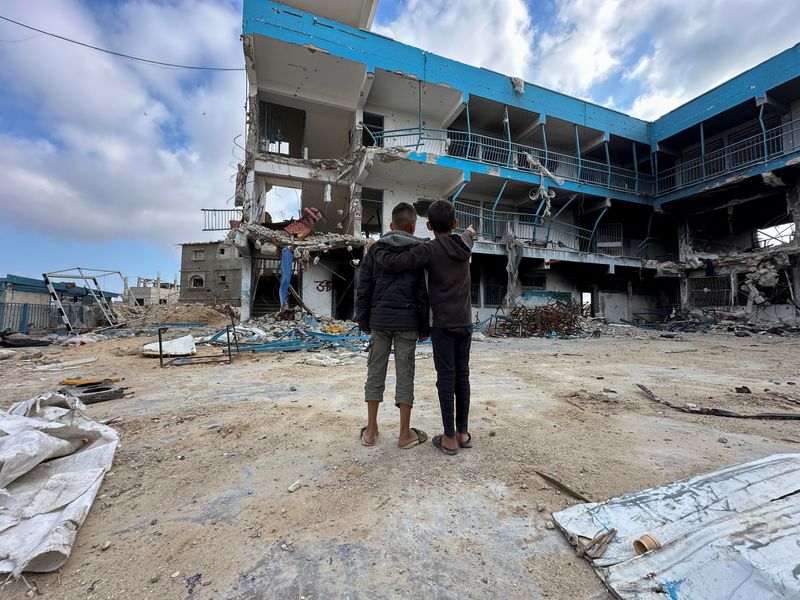 &copy; Reuters. Los escolares palestinos Abed Al-Qara y Muhammad Al-Fajem ven su escuela que fue destruida durante la ofensiva militar de Israel, en medio del conflicto en curso entre Israel y Hamás, en Jan Yunis en el sur de la Franja de Gaza. 14 de abril de 2024. REUT