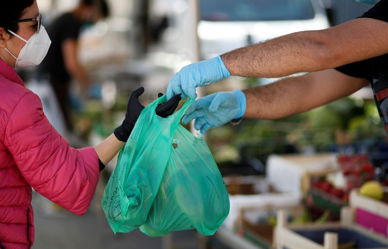 © Reuters. FILE PHOTO: A vendor delivers a plastic bag at an open-air food market in Cisternino, Italy, April 27, 2020. REUTERS/Alessandro Garofalo/File Photo