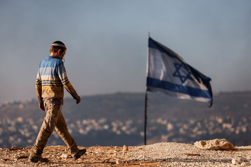 &copy; Reuters. FILE PHOTO: A Jewish settler teenager walks by an Israeli flag in Givat Eviatar, a new Israeli settler outpost, near the Palestinian village of Beita in the Israeli-occupied West Bank June 23, 2021. Picture taken June 23, 2021. REUTERS/Amir Cohen/File Pho