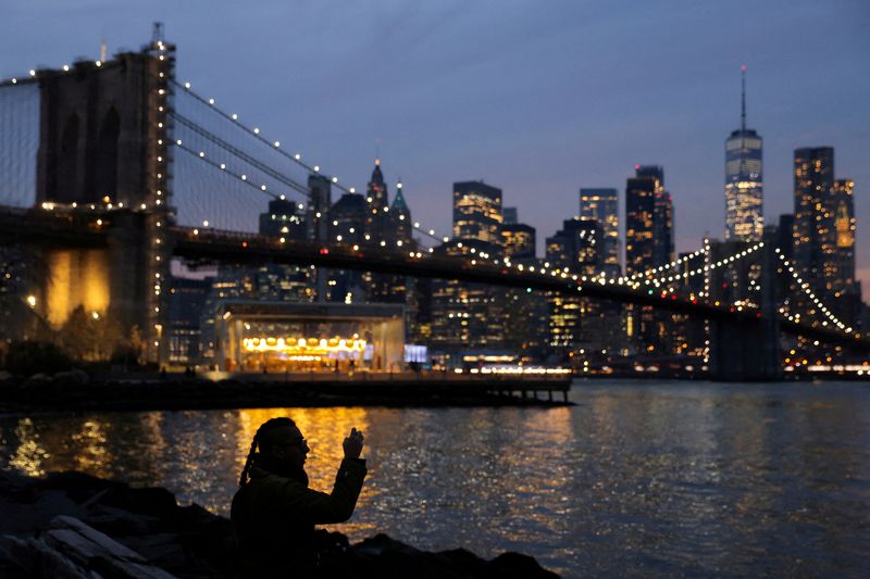 &copy; Reuters. Une personne prend une photo en regardant la ligne d'horizon de Manhattan lors du solstice d'hiver à Brooklyn, New York City, États-Unis. /Photo prise le 21 décembre 2021/REUTERS/Andrew Kelly