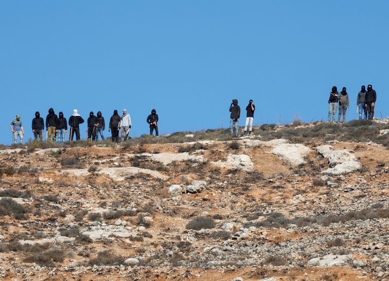 &copy; Reuters. FILE PHOTO: Israeli settlers watch from a distance as Israeli soldiers deny access to Palestinian farmers to harvest olives, in Burqa near Ramallah in the Israeli-occupied West Bank October 20, 2024. REUTERS/Mohammed Torokman/File Photo