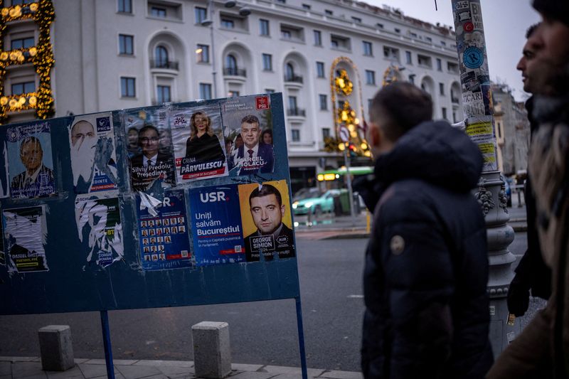 © Reuters. People walk past a poster depicting Prime Minister Marcel Ciolacu and the leader of the radical right Alliance for Uniting Romanians (AUR) George Simion, a day before parliamentary elections, in Bucharest, Romania, November 30, 2024. REUTERS/Alkis Konstantinidis