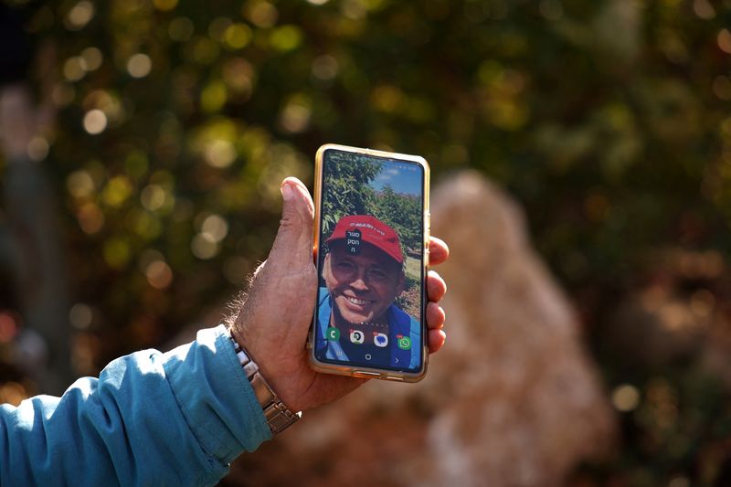 © Reuters. Moshe Weinstein, 76, an Israeli farmer holds up his phone with a picture of his son Omer at the site of his killing by shrapnel from a rocket launched from Lebanon, at his apple farm in Metula, northern Israel, December 1, 2024. REUTERS/Stoyan Nenov