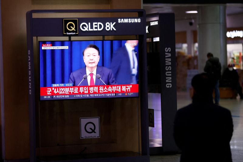 &copy; Reuters. A person watches a TV screen broadcasting a news report on South Korean President Yoon Suk Yeol's declaration of martial law and the following announcement that he will lift the martial law, after parliamentary vote, at a railway station in Seoul, South K