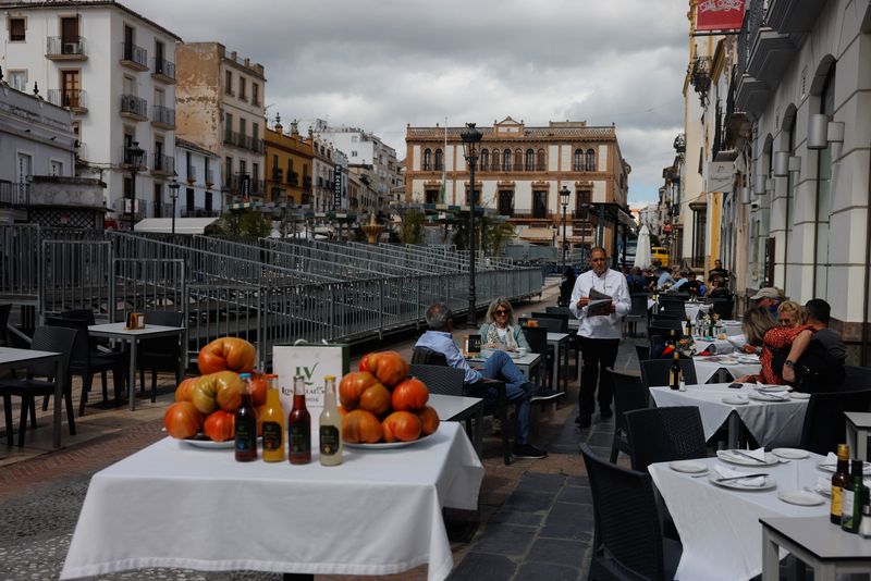 © Reuters. FILE PHOTO: A waiter serves tourists at the terrace of a restaurant in front of an official stand, installed to watch the Holy Week processions, in Ronda, Spain, March 14, 2024. REUTERS/Jon Nazca/File Photo