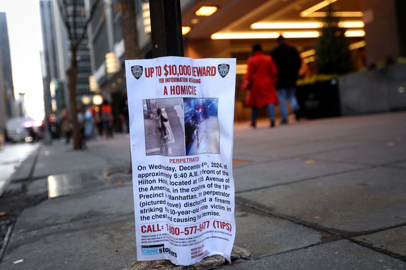 © Reuters. People walk next to a poster outside the Hilton hotel near the scene where the CEO of UnitedHealthcare Brian Thompson was shot dead in Midtown Manhattan, in New York City, U.S., December 5, 2024. REUTERS/Mike Segar