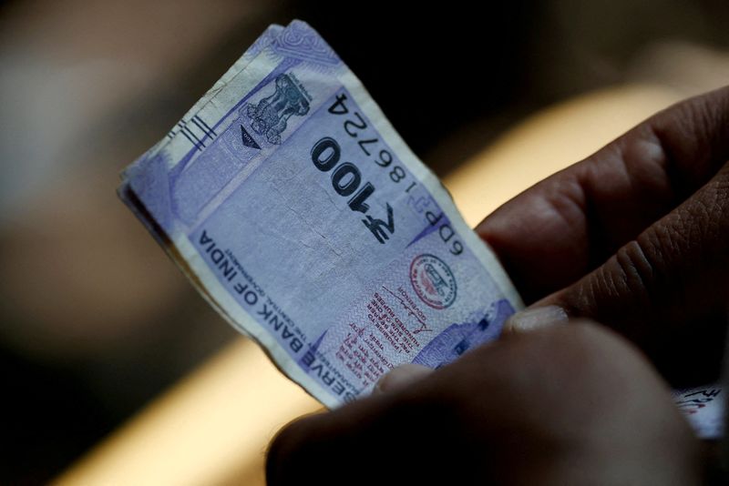 &copy; Reuters. FILE PHOTO: A customer holds hundred rupees Indian currency notes near a roadside currency exchange stall in New Delhi, India, May 24, 2024. REUTERS/Priyanshu Singh/File Photo