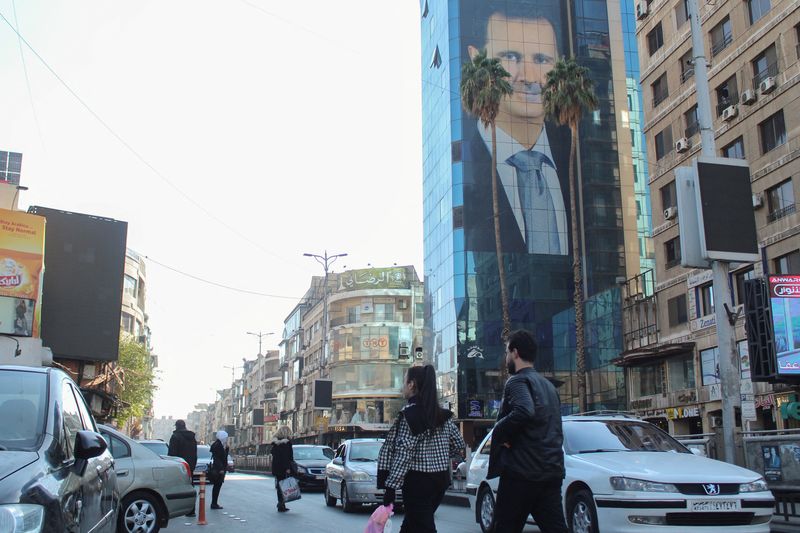 © Reuters. People walk near a poster depicting Syria's President Bashar al-Assad in Damascus, after last week's rebel seizure of Aleppo marked the biggest offensive for years, Syria December 5, 2024. REUTERS/Firas Makdesi/File Photo