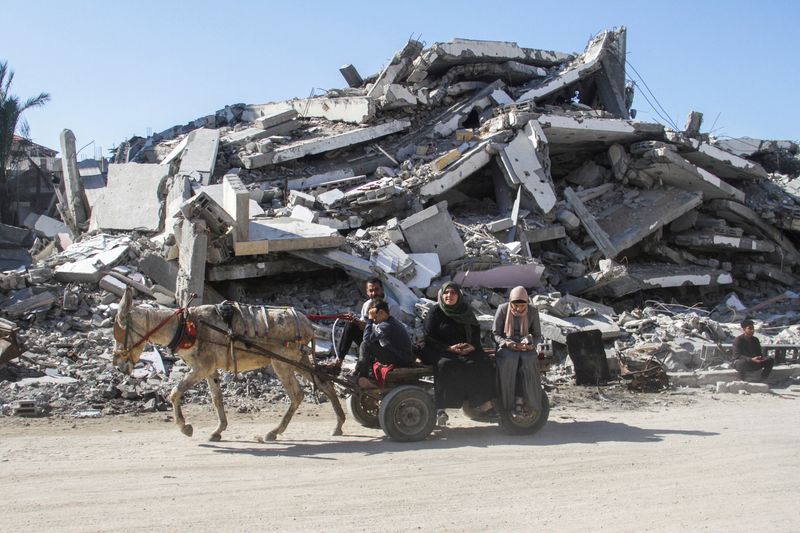 © Reuters. Palestinians ride a donkey cart past the rubble before a ceasefire between Israel and Hamas takes effect, in Gaza City, January 19, 2025. REUTERS/Mahmoud Issa   