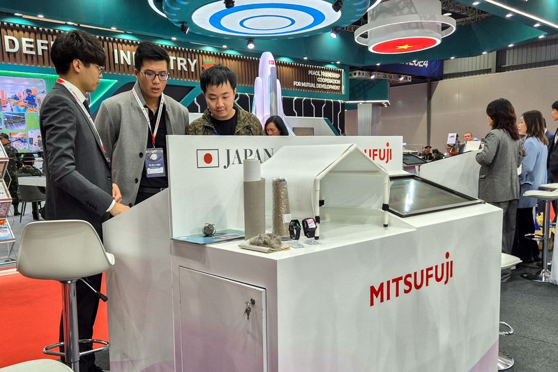 © Reuters. Staff members of Japanese firm Mitsufuji stand near to a small-scale model of a prototype hangar tent for electromagnetic shielding and wearable gadgets at the Vietnam Defence Expo 2024 in Hanoi, Vietnam, December 19, 2024. REUTERS/Khanh Vu