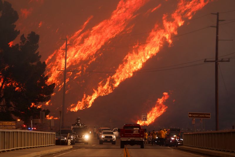 © Reuters. Flames rise behind vehicles as the Hughes Fire burns in Castaic Lake, California, U.S. January 22, 2025. REUTERS/David Swanson     