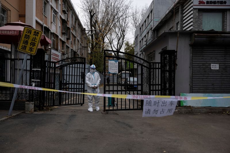 © Reuters. FILE PHOTO: An epidemic-prevention worker in a protective suit stands guard at the gate of a residential compound as coronavirus disease (COVID-19) outbreaks continue in Beijing, China November 28, 2022. REUTERS/Thomas Peter/File Photo