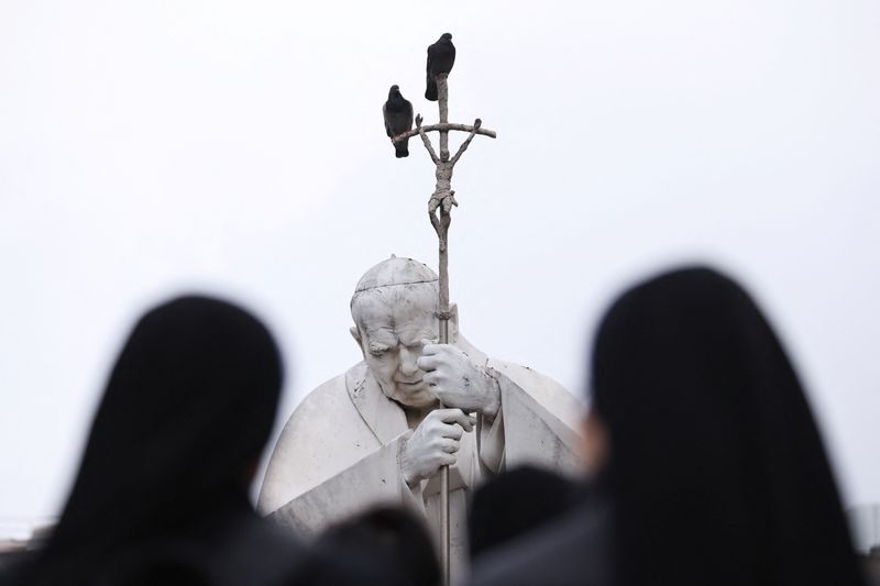 &copy; Reuters. Estátua do falecido papa João Paulo 2º com pessoas rezando do lado de fora do Hospital Gemelli, onde o papa Francisco está internado em Roman 25/2/2025     REUTERS/Claudia Greco